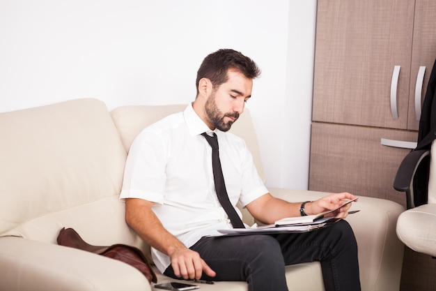 Hombre de negocios que trabaja en la oficina en el sofá poniendo largas horas de trabajo. Empresario en entorno profesional