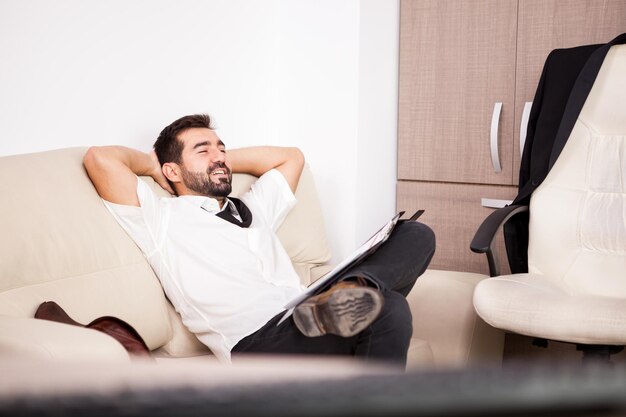 Hombre de negocios que trabaja en la oficina en el sofá poniendo largas horas de trabajo. Empresario en entorno profesional