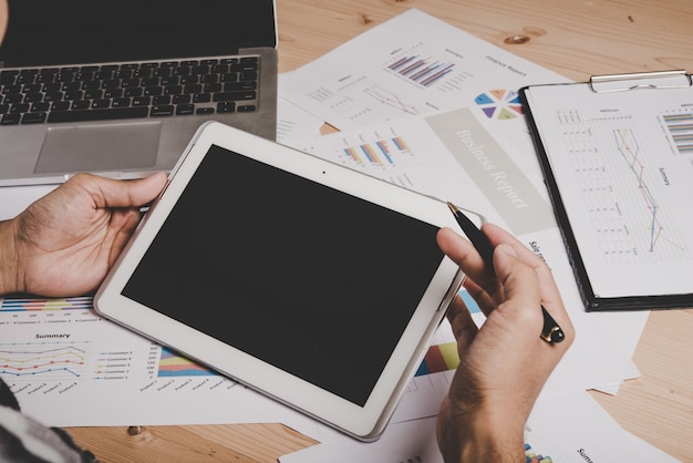 Hombre de negocios que trabaja con la pantalla en blanco tableta digital y portátil en el escritorio de madera en la oficina.