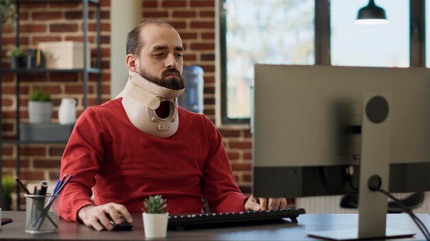 Hombre de negocios que usa cuello para recuperarse de una lesión física, trabajando en gráficos y gráficos de estrategia financiera. Empleado de oficina usando espuma cervical para curar fracturas en el trabajo.