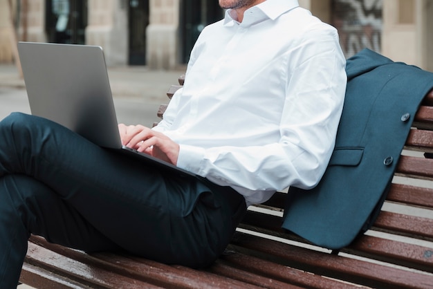 Hombre de negocios relajado que se sienta en banco usando el ordenador portátil