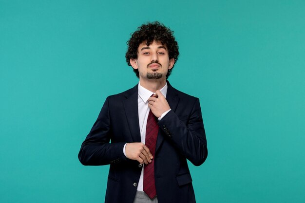 Hombre de negocios rizado lindo chico guapo en traje negro atando una corbata roja