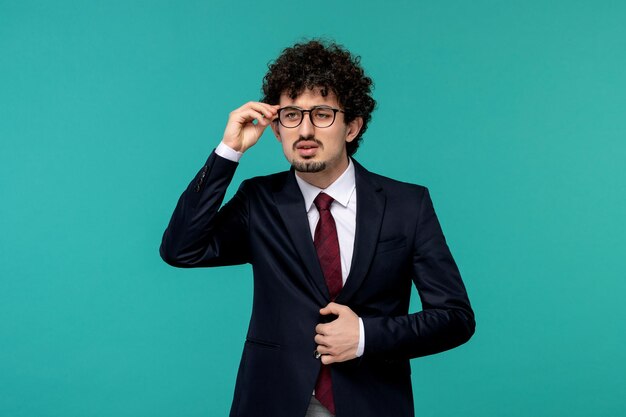 Hombre de negocios rizado lindo chico guapo en traje negro y corbata roja pensando y con gafas