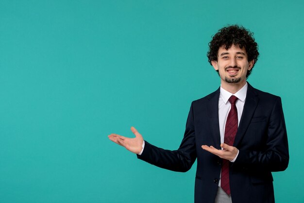 Hombre de negocios rizado lindo chico guapo en traje negro y corbata roja sonriendo y apuntando a la izquierda