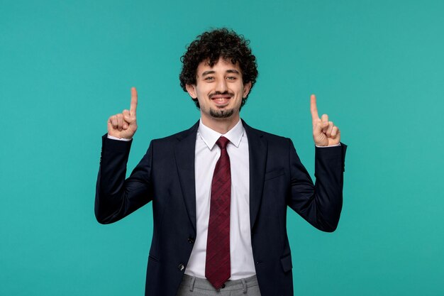 Hombre de negocios rizado lindo chico guapo en traje negro sonriendo y apuntando hacia arriba