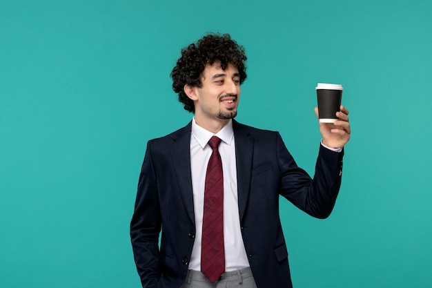 Hombre de negocios rizado lindo chico guapo en traje negro sosteniendo una taza de café y sonriendo