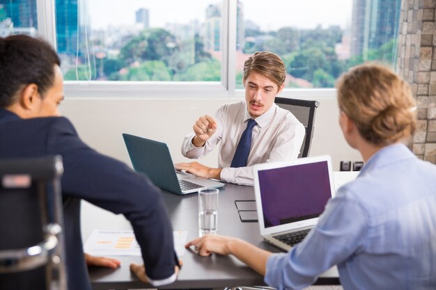 Hombre de negocios sentado con un portátil hablando a otros compañeros