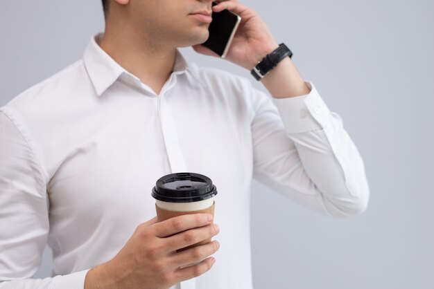 Hombre de negocios serio con café para llevar que habla en el teléfono móvil