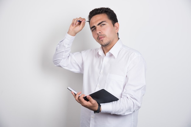 Hombre de negocios serio con cuaderno posando sobre fondo blanco.