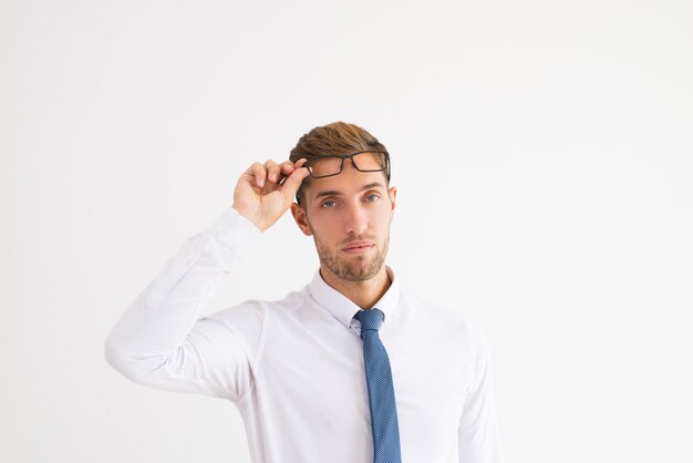 Hombre de negocios serio levantando gafas y mirando a cámara