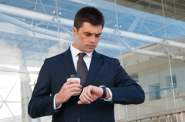 Hombre de negocios serio que comprueba tiempo en el reloj al aire libre