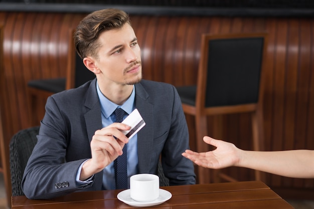 El hombre de negocios serio que da la tarjeta al camarero en el Café