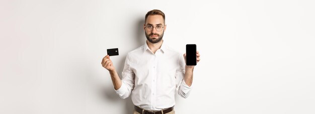 Hombre de negocios serio que muestra la pantalla móvil y el concepto de tarjeta de crédito de compras en línea