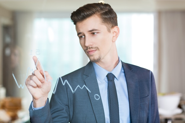 El hombre de negocios serio que señala al gráfico de vidrio