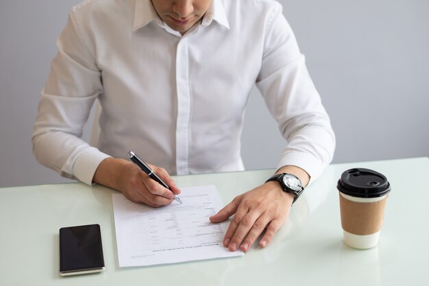 Hombre de negocios serio que se sienta en la mesa y que completa la aplicación