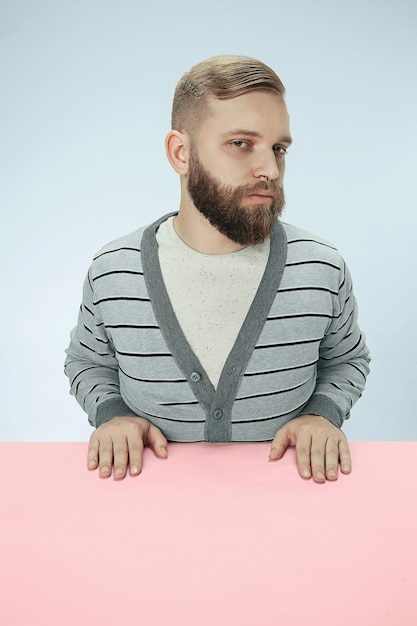 Hombre de negocios serio sentado a la mesa sobre fondo azul de estudio.