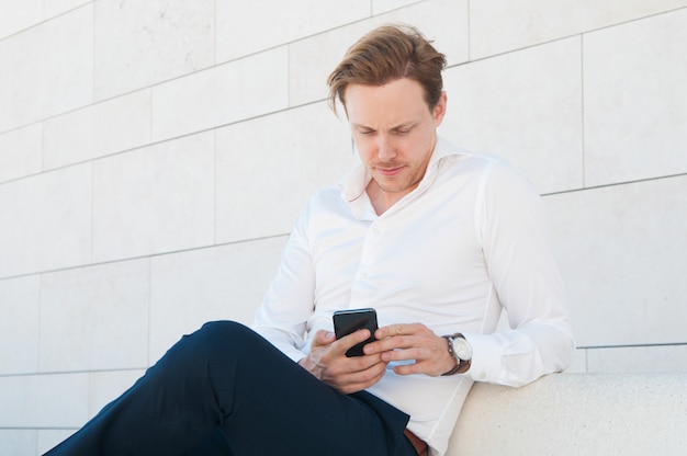 Hombre de negocios serio con smartphone en banco al aire libre