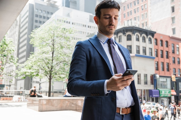 Foto gratuita hombre de negocios serio con teléfono inteligente en la calle