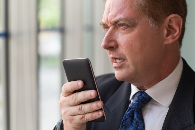 Hombre de negocios serio usando la grabadora de voz en el teléfono