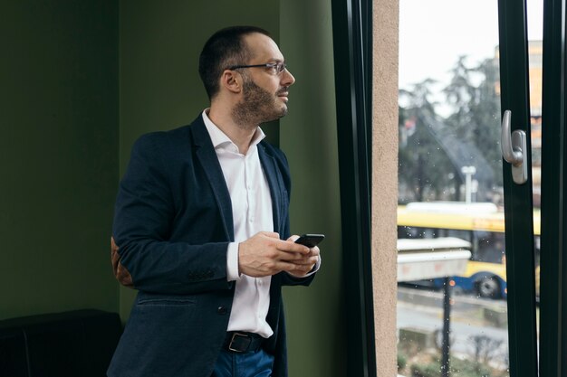 Hombre de negocios con smartphone mirando por la ventana