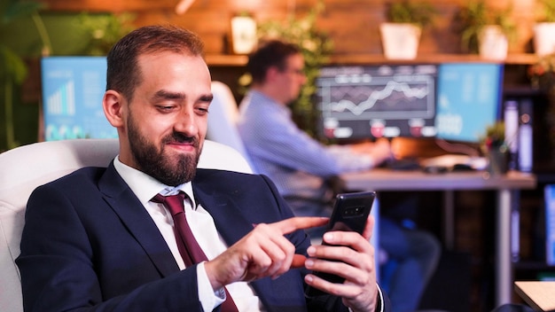 Hombre de negocios sonriendo y mirando su teléfono inteligente. Colega trabajando en la espalda