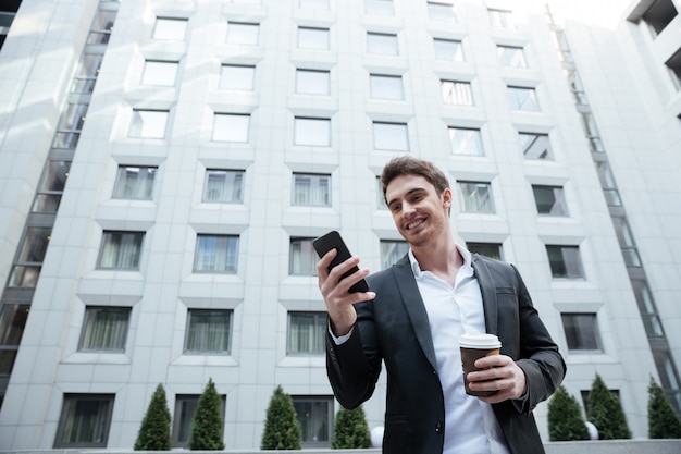 Hombre de negocios sonriente con café con smartphone en centro de negocios