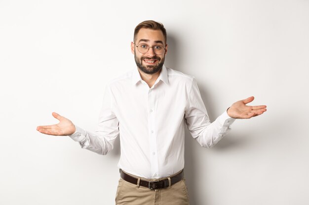 Hombre de negocios sonriente confundido no sé, encogiéndose de hombros y diciendo lo siento, de pie