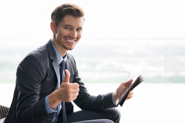 Hombre de negocios sonriente joven con el pulgar hacia arriba y Tablet