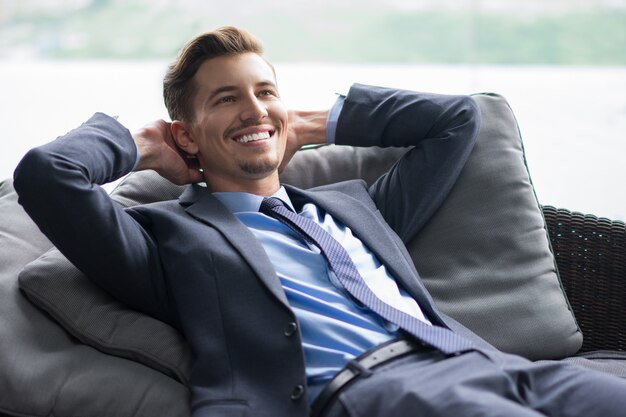 El hombre de negocios sonriente con las manos detrás de la cabeza en el sofá