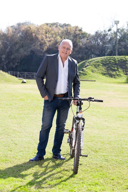 Hombre de negocios sonriente posando con su bicicleta en el parque