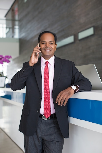 Hombre de negocios sonriente que llama en el teléfono en la recepción