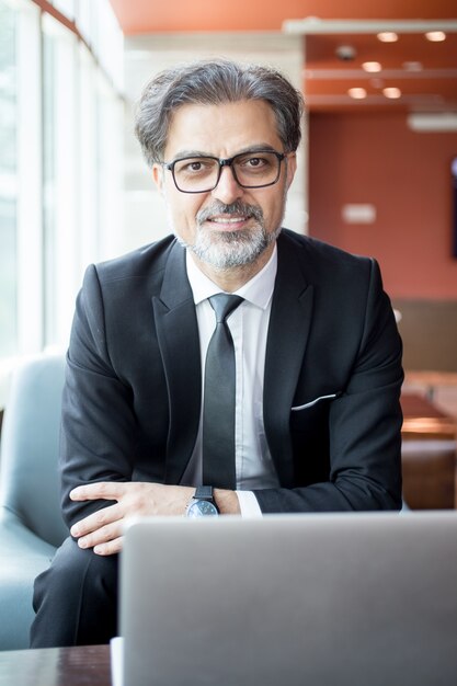 Hombre de negocios sonriente que se sienta en la tabla con la computadora portátil