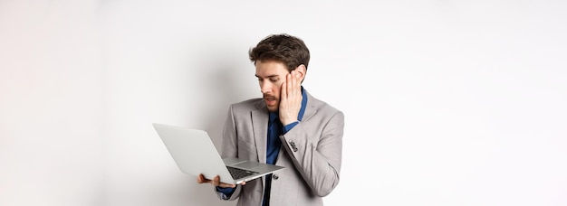 Hombre de negocios sorprendido y preocupado cometiendo un error en la computadora portátil mirando la computadora molesta de pie en blanco