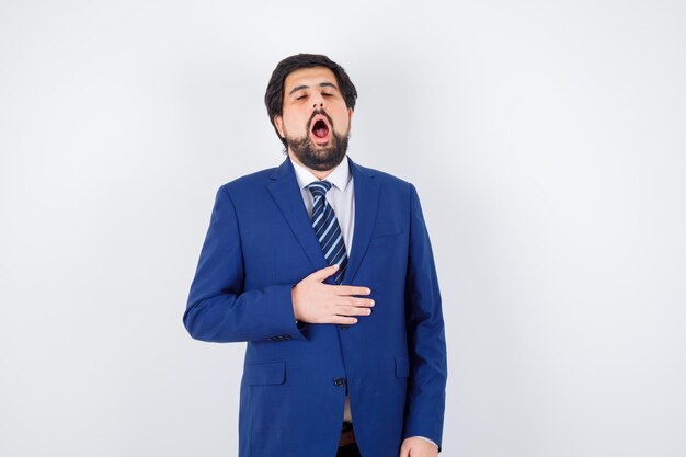 Hombre de negocios sosteniendo la mano en la chaqueta, bostezando en traje formal y con sueño. vista frontal.