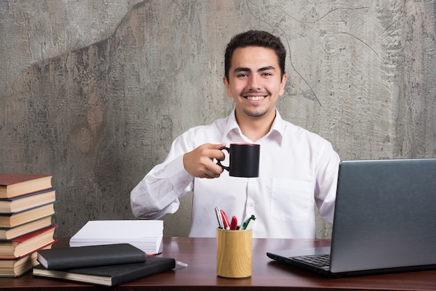 Hombre de negocios con taza de té sonriendo en el escritorio de oficina.