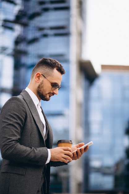 Hombre de negocios con teléfono bebiendo café fuera de rascacielos