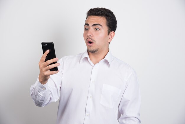 Hombre de negocios con teléfono mirando consternado sobre fondo blanco.