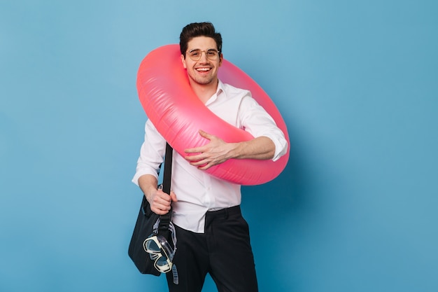 Foto gratuita hombre de negocios en traje blanco y negro y gafas sonríe mientras sostiene el anillo de goma y la máscara de buceo.