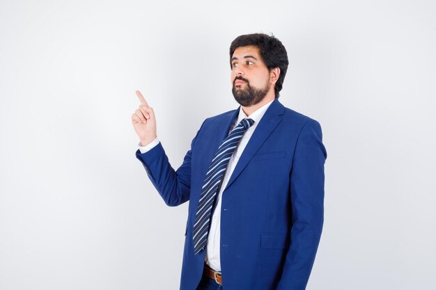 Hombre de negocios en traje formal apuntando hacia arriba y mirando serio, vista frontal.