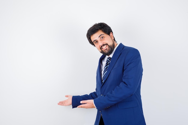 Hombre de negocios en traje formal estirando las manos hacia la izquierda y sonriendo y mirando feliz, vista frontal.