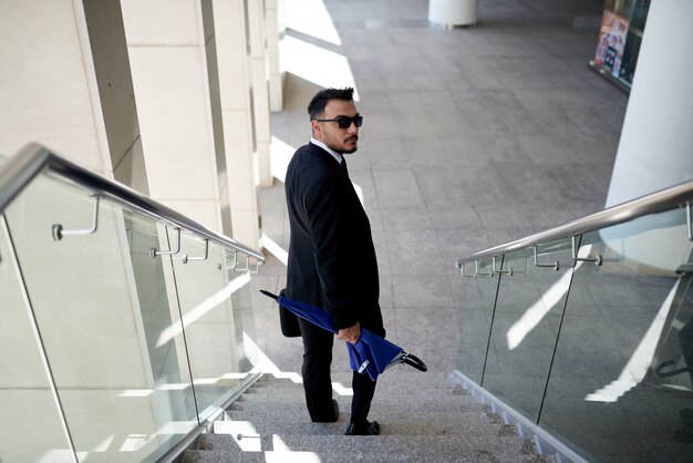 Hombre de negocios en traje y gafas de sol caminando por la escalera y mirando a la cámara