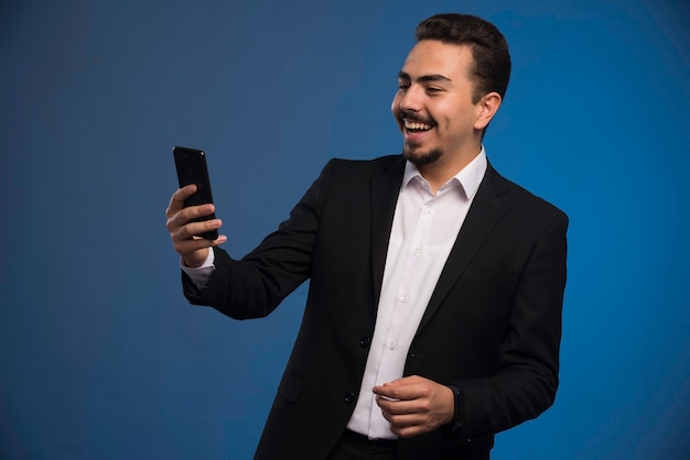 Hombre de negocios en traje negro comprobando su teléfono.