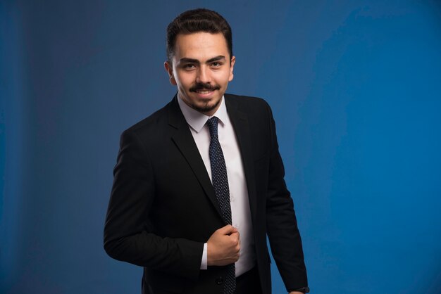 Hombre de negocios en traje negro con corbata posando positivo.