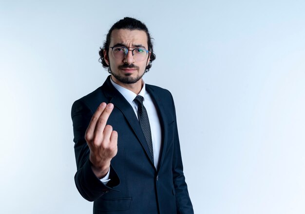 Hombre de negocios en traje negro y gafas mirando al frente con rostro serio mostrando dos dedos de pie sobre la pared blanca