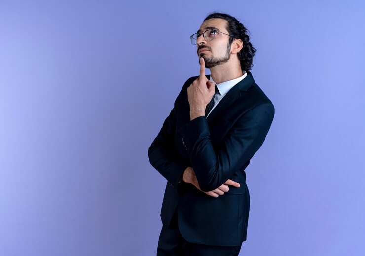 Foto gratuito hombre de negocios en traje negro y gafas mirando desconcertado parado sobre la pared azul
