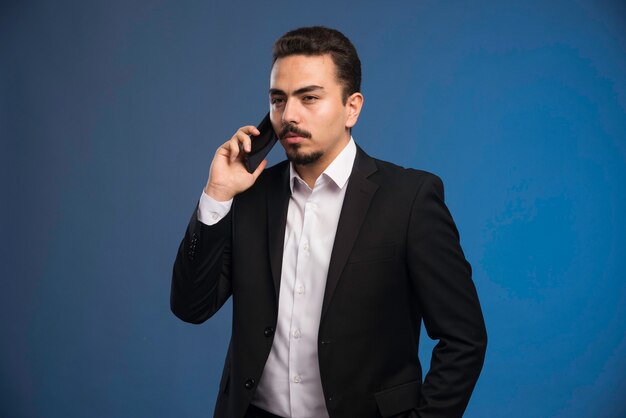 Hombre de negocios en traje negro hablando por teléfono.