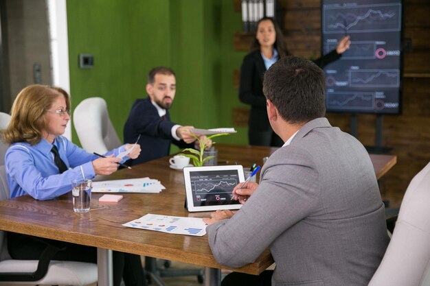 Hombre de negocios en traje trabajando en tableta con gráficos en la sala de conferencias. Lluvia de ideas del equipo