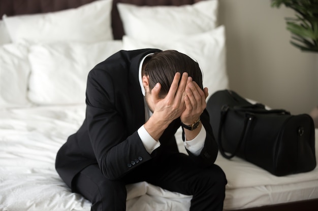 Hombre de negocios trastornado subrayado que se sienta en cama, teniendo dolor de cabeza.