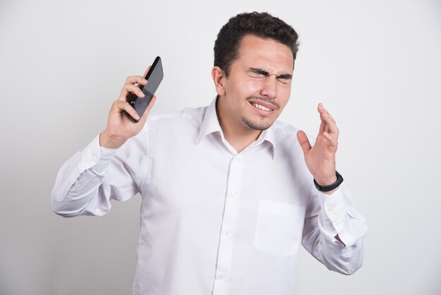 Hombre de negocios tratando de alejarse del teléfono sobre fondo blanco.