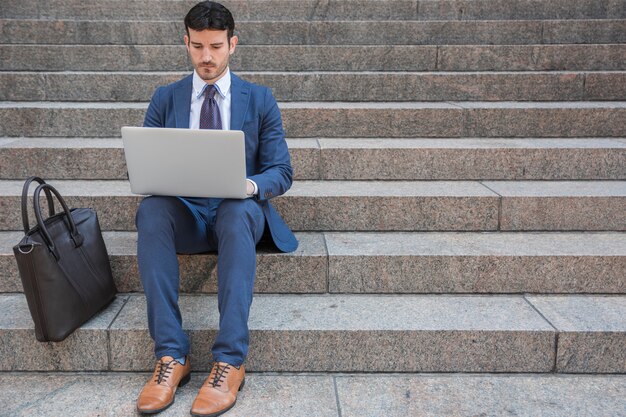 Hombre de negocios usando la computadora portátil cerca de bolsa